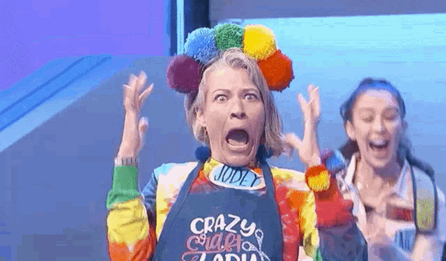 a woman wearing a tie dye shirt and an apron is making a funny face with her mouth open .