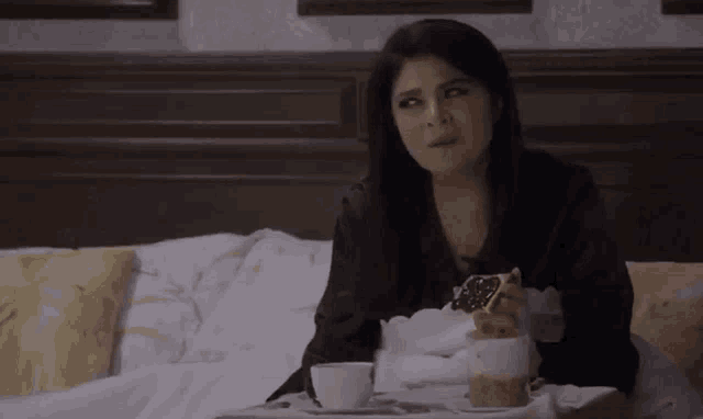 a woman is sitting on a bed with a tray of food and a cup of coffee .