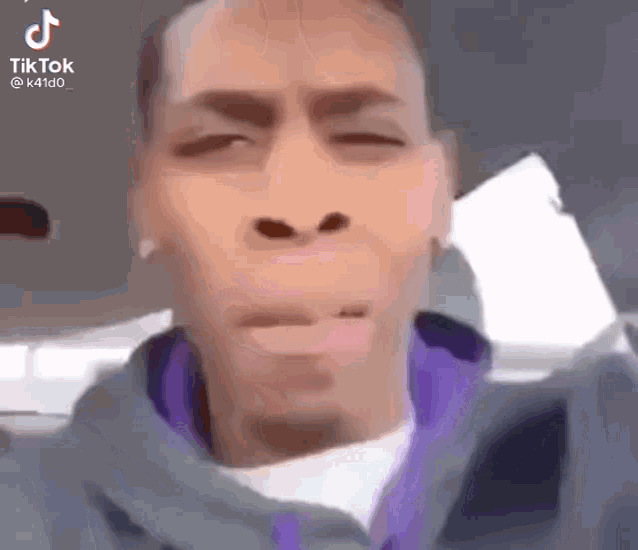 a man in a purple jacket is making a funny face while sitting in a car .