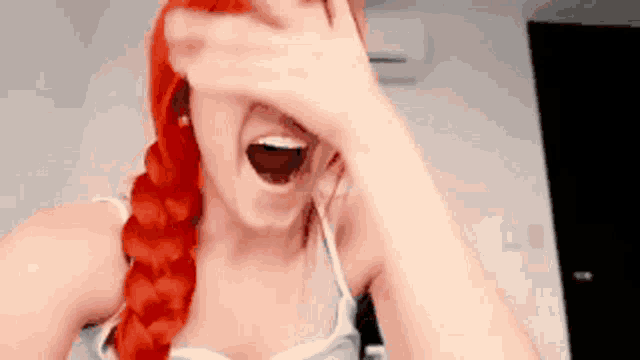 a woman with red hair is covering her face with her hand .