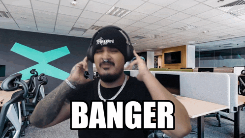 a man wearing headphones and a beanie says banger in an office