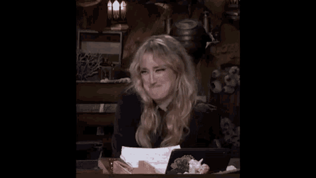 a woman is sitting at a table with her hands in her pockets and her hair blowing in the wind .