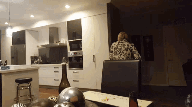 a woman sits at a table in a kitchen with a bottle of wine and a plate that says " christmas " on it