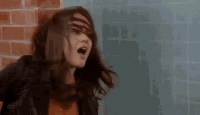 a woman is standing in front of a brick wall with her mouth open and her hair blowing in the wind .