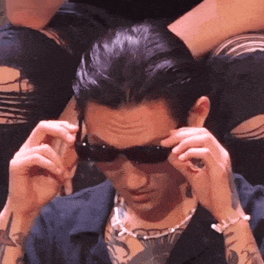 a man wearing sunglasses and a necklace has a tattoo on his arm