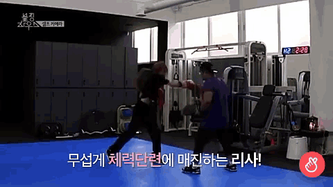 a man in a purple shirt is boxing another man in a gym with a digital clock that reads 2:26
