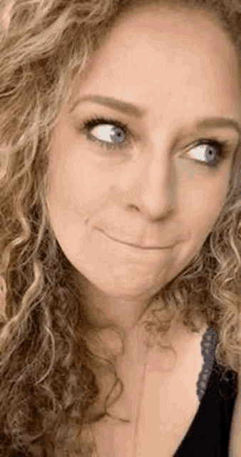 a close up of a woman 's face with curly hair making a funny face .