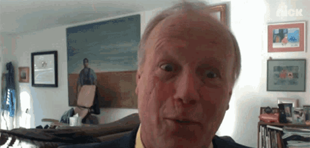 a man in a suit and yellow shirt is looking at the camera in front of a wall with pictures on it and a sign that says nick