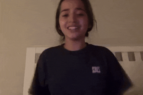 a young girl wearing a black t-shirt is standing next to a bed .