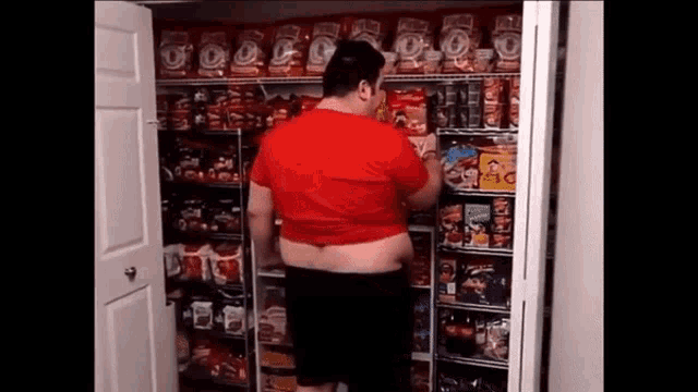 a man in a red shirt is standing in front of a shelf full of snacks including doritos