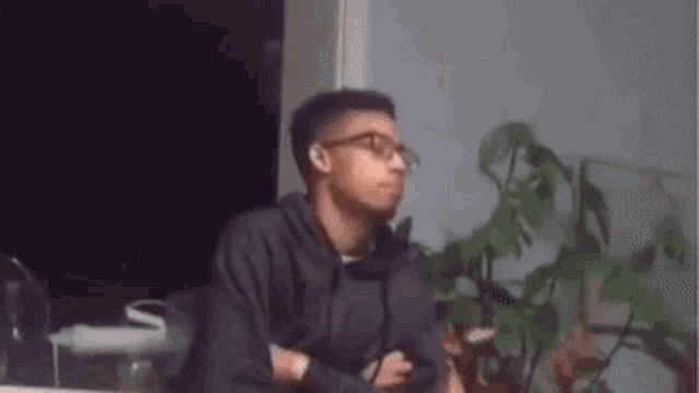 a man wearing glasses and a hoodie is sitting in a dark room .