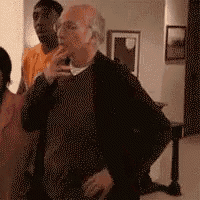 a man in a black sweater is standing in a living room with a group of people .