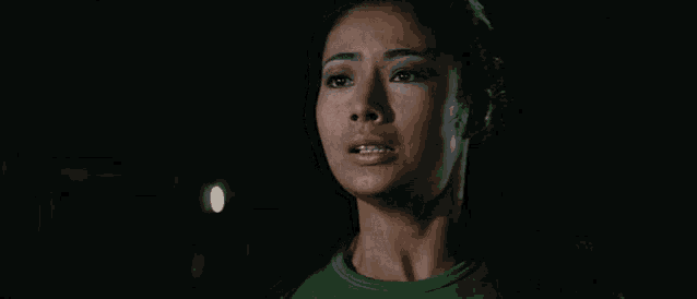 a woman in a green shirt is standing in a dark room .