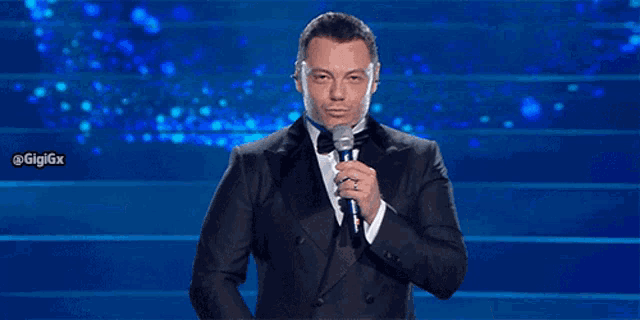 a man in a tuxedo and bow tie is holding a microphone