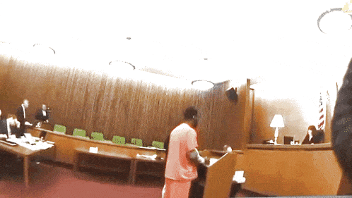 a man stands at a podium in a courtroom with a flag on the wall behind him