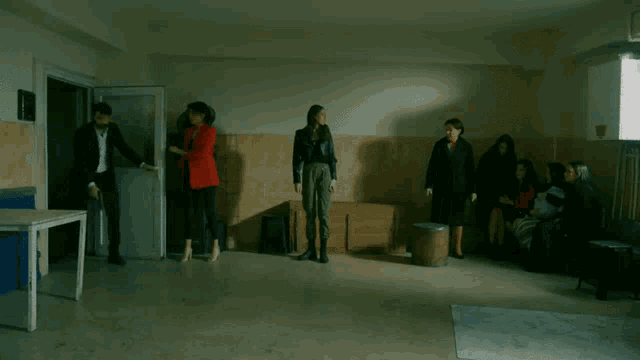 a group of people are standing in a room and one of them is wearing a red top