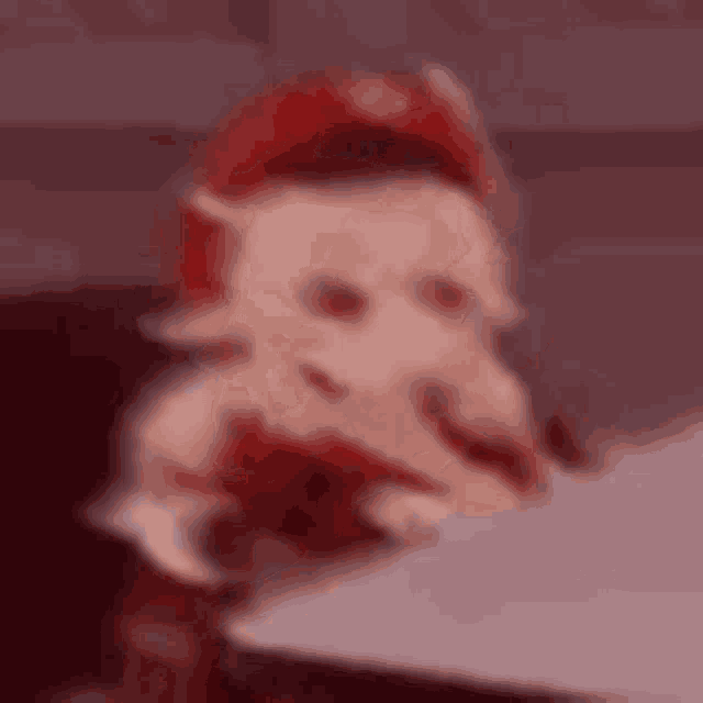 a blurred image of a doll sitting at a table with a red hat on .