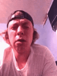 a man wearing a baseball cap and a white shirt is making a face .