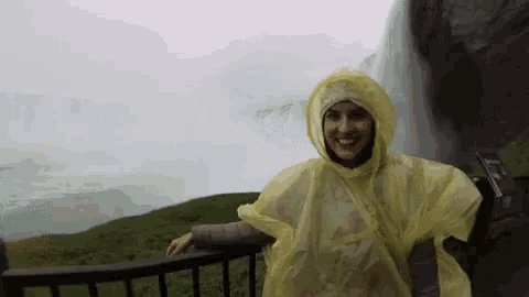 a woman wearing a yellow poncho is standing in front of a waterfall .