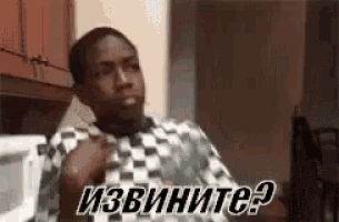 a man in a checkered shirt is sitting in a kitchen with a microwave in the background .