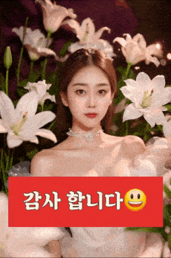 a woman in a white dress is surrounded by white flowers and a red sign that says " 감사 합니다 "