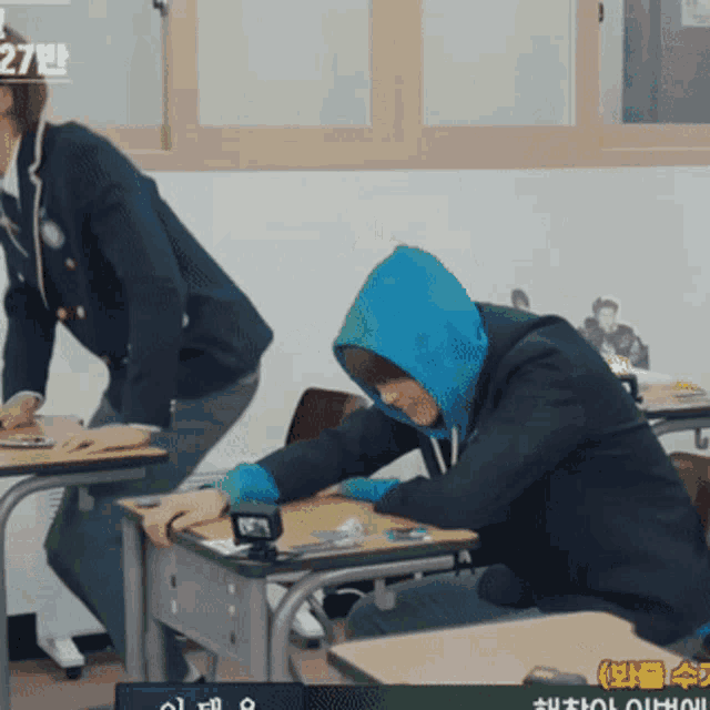 a man wearing a blue hoodie is sitting at a desk in a classroom