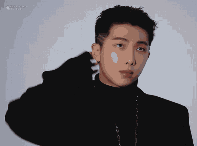 a man wearing a black turtleneck and a chain around his neck is looking at the camera