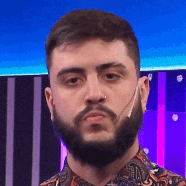 a man with a beard and a nose ring is wearing a paisley shirt and making a funny face .