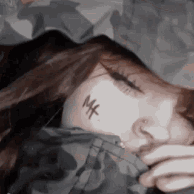 a woman with a tattoo on her face is sleeping with her eyes closed and covering her face with a jacket .