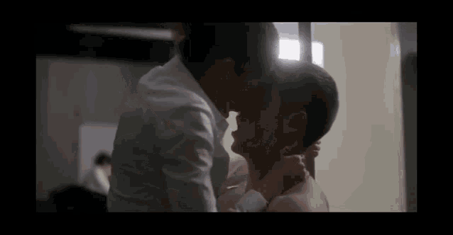 a man in a white shirt is kissing another man without a shirt on .
