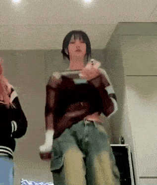 a woman is standing in a room holding a cell phone and dancing .