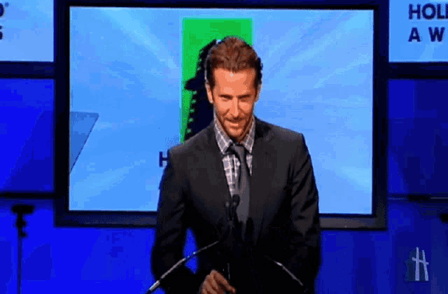 a man in a suit is giving a speech in front of a screen that says holiday awards