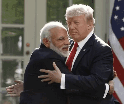 two men in suits and ties are hugging each other in front of an american flag .