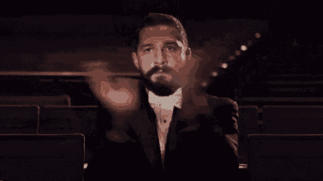 a man with a beard in a tuxedo and bow tie holds a baton