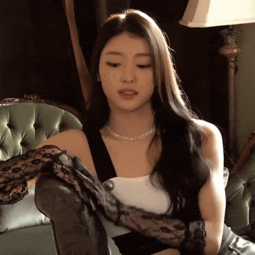 a woman wearing black lace gloves and a necklace is sitting on a chair
