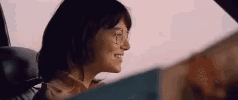 a woman wearing glasses is driving a car and smiling .