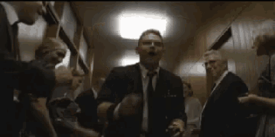 a man in a suit and tie is standing in a hallway surrounded by other people .
