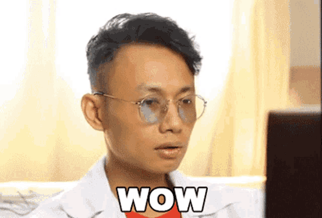 a man wearing glasses is sitting in front of a laptop with the word wow on his face