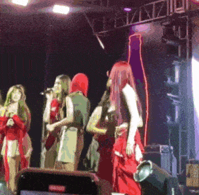 a group of women singing on a stage in front of a coca cola bottle