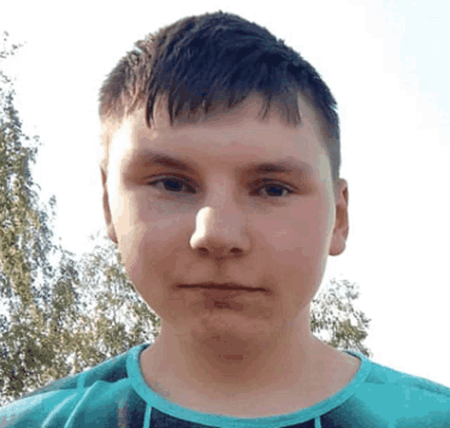 the boy is wearing a blue shirt and looking at the camera .
