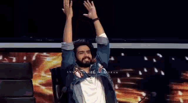 a man with a beard is sitting in a chair with his hands up in the air .