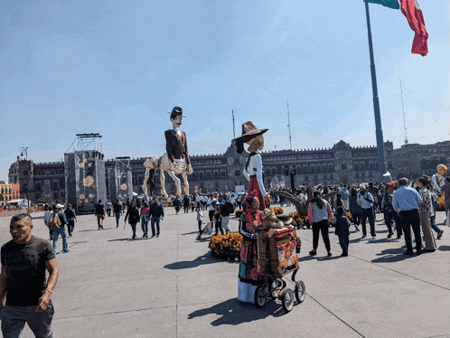 a group of people are gathered in a plaza with a giant skeleton statue in the background
