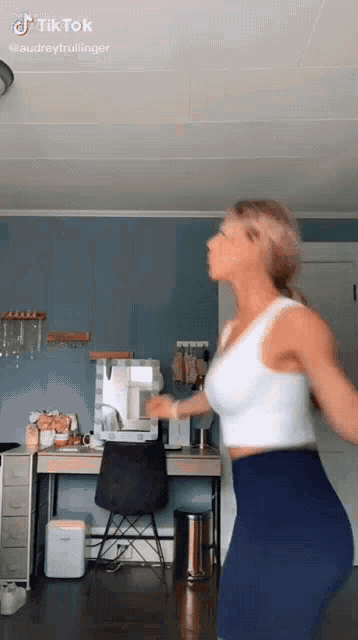 a woman is dancing in a room with a desk and chair .
