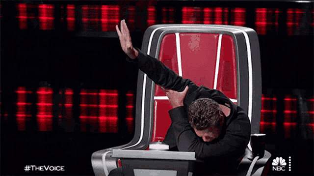 a man is sitting in a chair with his arms outstretched in front of a screen that says nbc
