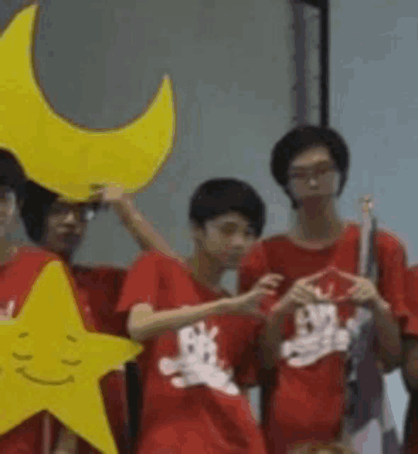 a group of young people in red shirts are standing next to each other holding a yellow star and a yellow crescent moon .