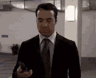 a man in a suit and tie is walking down a hallway holding a cell phone in his hand .