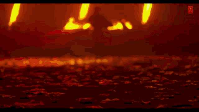 a silhouette of a man standing in front of a fire with a t on the bottom right