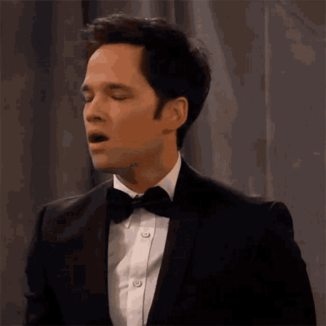 a man in a tuxedo and bow tie is making a surprised face .