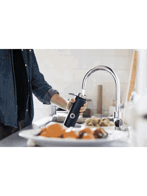 a person is washing vegetables in a kitchen sink and holding a black bottle with an o on it