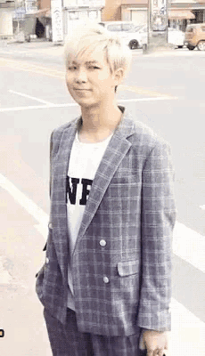 a man wearing a plaid jacket and a white shirt with the letter nf on it is standing on a street .